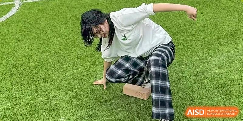 A student in a white shirt and plaid trousers balances on a wooden block during a field challenge at Griffin International Academy.