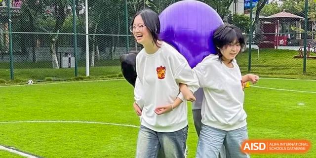 Two female students laugh while carrying a large purple exercise ball during a house sports competition at Griffin International Academy.