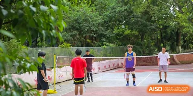 A student in a red shirt prepares to serve during an outdoor badminton match on the campus courts at Griffin International Academy.