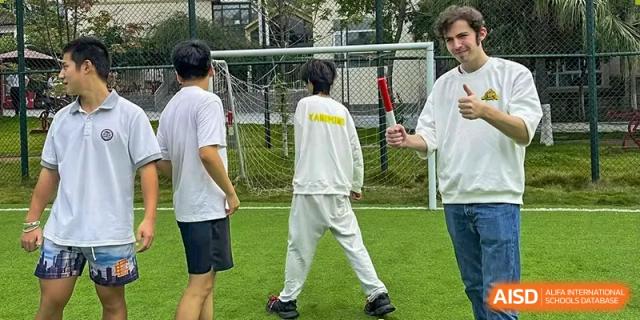 Two students engage in a team-building exercise involving a red baton on the school field at Griffin International Academy.