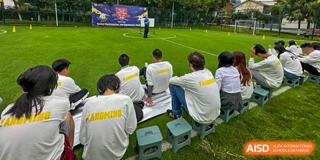 A group of students in white shirts sits on the grass and watches an outdoor presentation at Griffin International Academy.