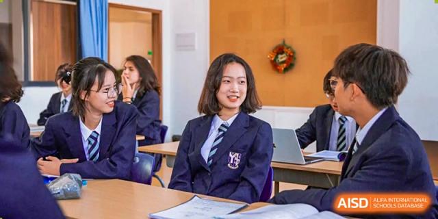 A young female student in a formal navy school uniform smiles while sitting in a bright classroom during a lesson at St Bees Dongguan.
