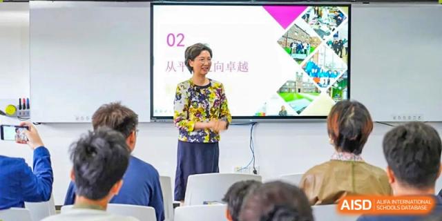 A female educator in a floral top leads an interactive seminar for a group of students using a large display screen at St Bees Dongguan.