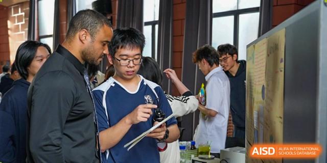 A male student in a blue polo shirt takes notes on a clipboard while observing a science experiment in a school laboratory at St Bees Dongguan.