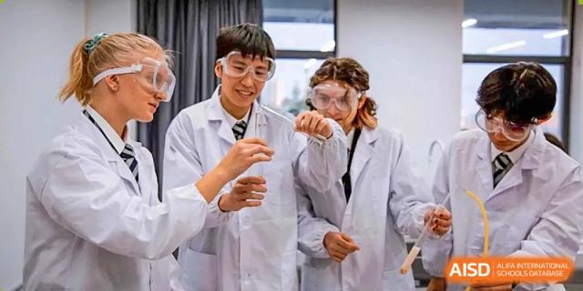 A group of students wearing protective lab goggles work together on a chemistry experiment involving test tubes and orange liquids at St Bees Dongguan.