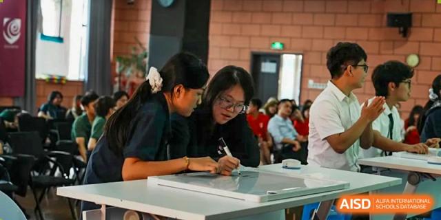 Two female students in school uniforms focus intently on a collaborative writing or drawing task at a table in a modern learning space at St Bees Dongguan.