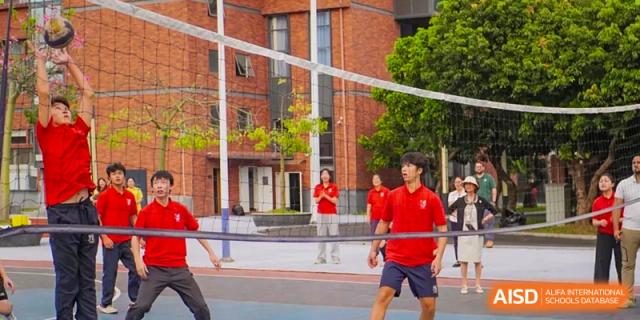 Students in red and blue athletic wear participate in an energetic game of volleyball on an outdoor court at St Bees Dongguan.