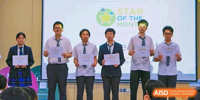 Three male students in formal uniforms stand together on a stage holding "Star of the Month" certificates during an awards ceremony at St Bees Dongguan.