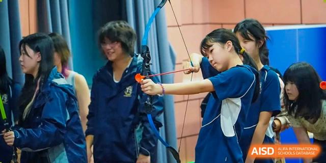 Two female students in school jackets practice their archery skills together under the guidance of an instructor at St Bees Dongguan.