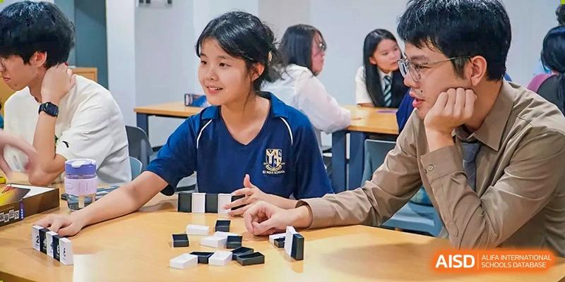 Two students sit at a table and play a game of dominoes during a social or extracurricular activity in a classroom at St Bees Dongguan.