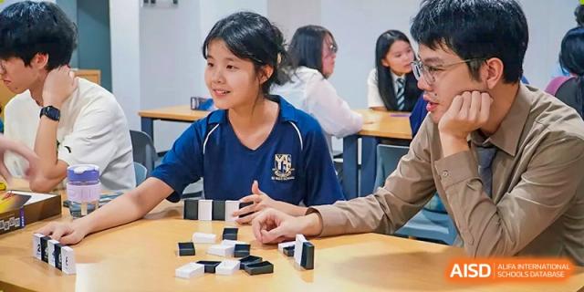 Two students sit at a table and play a game of dominoes during a social or extracurricular activity in a classroom at St Bees Dongguan.