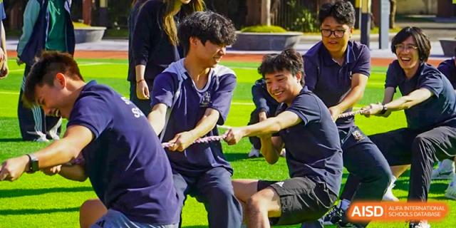 A group of students participate in a competitive game of tug-of-war on a green outdoor field during a school sports day at St Bees Dongguan.