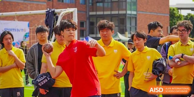 A male student in a red athletic shirt prepares to serve or catch a ball during an outdoor sports match on campus at St Bees Dongguan.