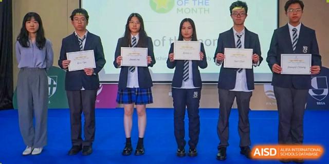 Three female students stand on a stage holding academic certificates during a "Star of the Month" recognition event at St Bees Dongguan.