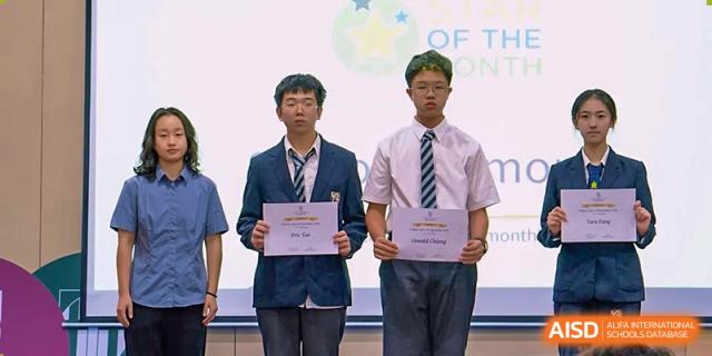 Two male students in formal school uniforms pose with their achievement certificates during an assembly on stage at St Bees Dongguan.