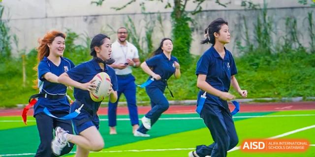 A female student in a navy athletic uniform runs across a green field while holding a ball during a sports match at St Bees Dongguan.