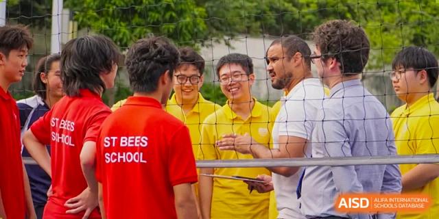 A group of students and a teacher in red and yellow shirts share a laugh while standing together outdoors at St Bees Dongguan.