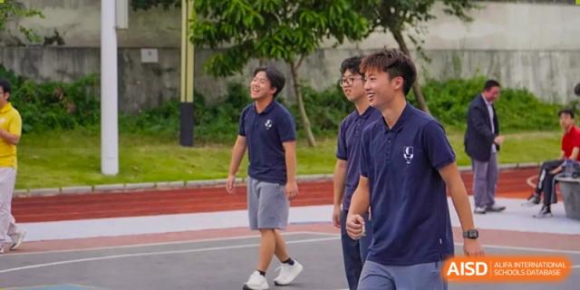 Three male students in navy polo shirts walk together and talk on an outdoor track during a break between classes at St Bees Dongguan.