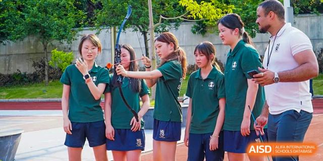 A group of female students in green school polo shirts practice their archery form together during an outdoor training session at St Bees Dongguan.