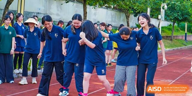 Students participate in a three-legged race on a red running track, smiling and linking arms while their ankles are tied with pink ribbons during a sports day event at St Bees Dongguan.