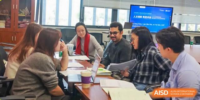 Educators collaborate on a curriculum project with laptops and papers in a meeting room at Beijing No. 35 High School International Department.