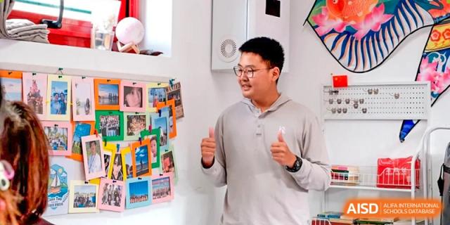 A student smiles while standing next to a creative wall of student-designed posters at Beijing No. 35 High School International Department.