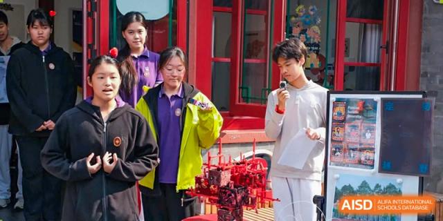 Two students in school uniforms address an audience from an outdoor stage with microphones at Beijing No. 35 High School International Department.