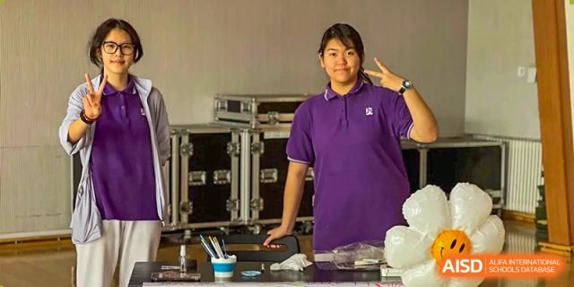 A student in a purple school shirt poses with a peace sign in front of event equipment at Beijing No. 35 High School International Department.