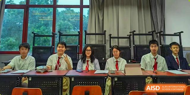 Three students in school uniforms sit at a desk for a group photo in a classroom at Beijing No. 35 High School International Department.