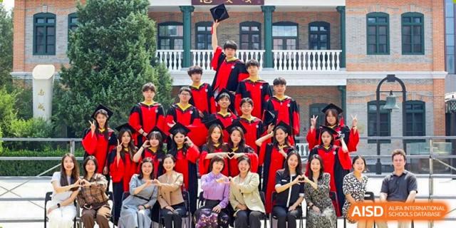 Graduates in black and red gowns pose for a large group photo on the steps of a traditional building at Beijing No. 35 High School International Department.