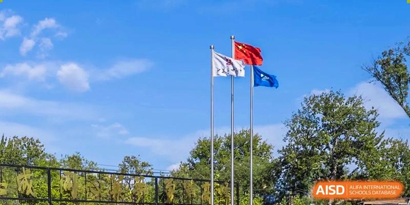 Three flags, including the national flag, fly high against a clear blue sky on the school grounds of Beijing No. 35 High School International Department.