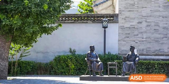 A bronze statue of a seated figure sits peacefully within a traditional courtyard at Beijing No. 35 High School International Department.
