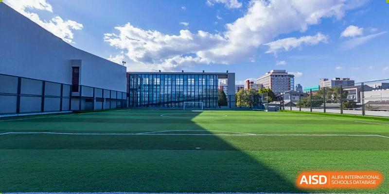 A wide-angle view of the lush green synthetic turf football field and modern school buildings at Beijing No. 35 High School International Department.