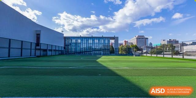 A wide-angle view of the lush green synthetic turf football field and modern school buildings at Beijing No. 35 High School International Department.