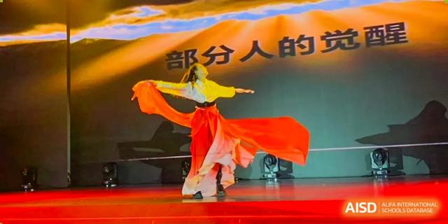 A solo dancer in a flowing orange and white traditional costume performs on stage at Beijing No. 35 High School International Department.