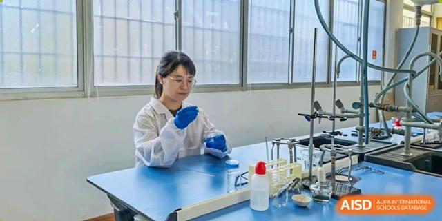 A student wearing safety gloves performs a hands-on science experiment using laboratory equipment at Xiamen ITG-SUIS High School