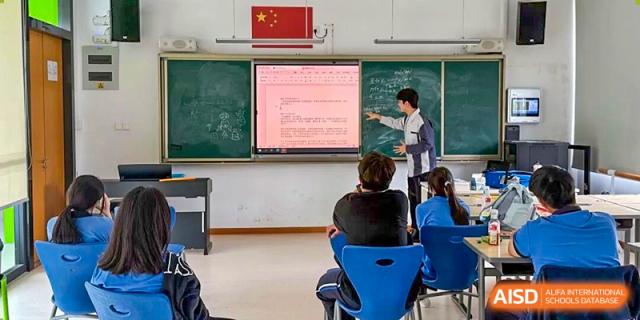 A teacher explains lesson material projected on a screen while students listen carefully in a structured classroom at Xiamen ITG-SUIS High School