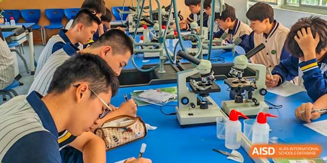 Students focus on scientific experiments using microscopes and lab tools during class at Xiamen ITG-SUIS High School