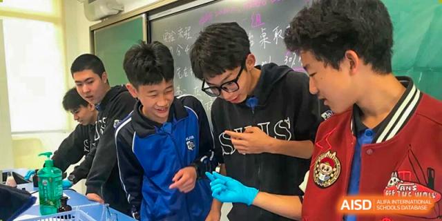 Students gather around a classmate during a science lesson, observing an experiment closely while discussing results in an engaging classroom setting at Xiamen ITG-SUIS High School