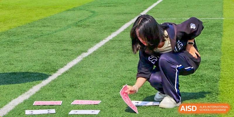 Student carefully placing a card on the sports field during a team-based outdoor activity, showing focus, coordination, and learning through physical challenges at Xiamen ITG-SUIS High School