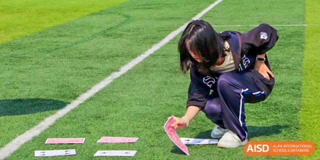 Student carefully placing a card on the sports field during a team-based outdoor activity, showing focus, coordination, and learning through physical challenges at Xiamen ITG-SUIS High School