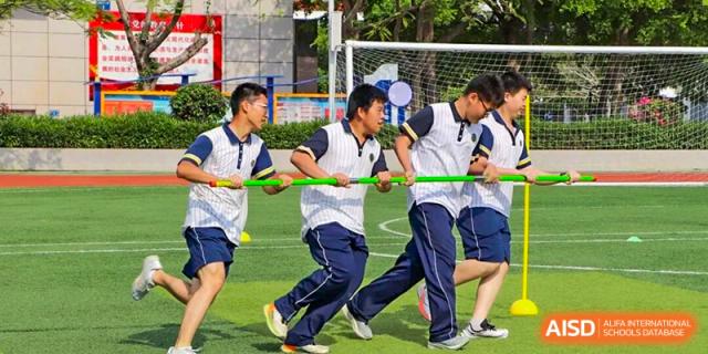 Students in sports uniforms working together to pass a pole during an outdoor team challenge, highlighting coordination, teamwork, and physical cooperation in a school sports activity at Xiamen ITG-SUIS High School