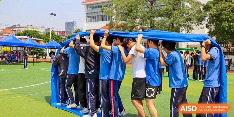 Group of students carrying a long board together during a collaborative outdoor exercise, building trust, balance, and communication skills in a physical education activity at Xiamen ITG-SUIS High School