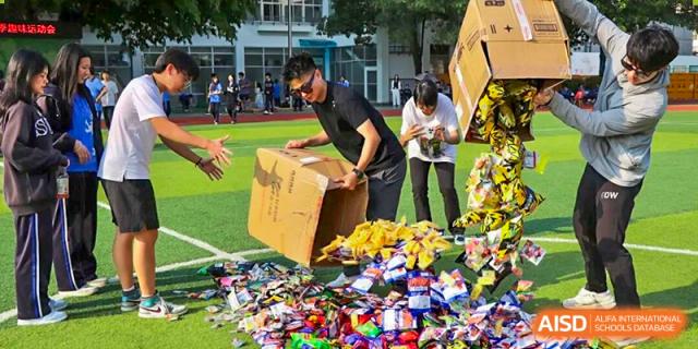 Students organizing and collecting snacks and supplies from a large box on the sports field during a fun school event, showing responsibility, teamwork, and active participation at Xiamen ITG-SUIS High School