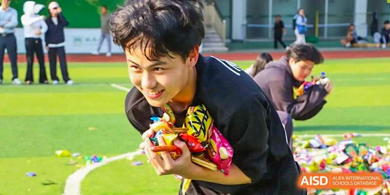 Student smiling while holding colorful snacks during an outdoor school activity, capturing joy, engagement, and energetic participation in a student-centered sports event at Xiamen ITG-SUIS High School