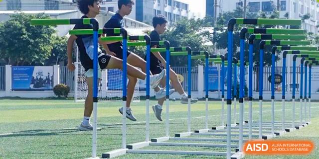 Students jumping over hurdles on the athletic field during a track and field exercise, demonstrating speed, focus, and physical fitness training as part of school sports activities at Xiamen ITG-SUIS High School