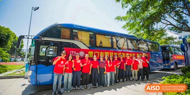 A group of students wearing matching red shirts stand proudly in front of a school bus during a group outing or school activity at Xiamen ITG-SUIS High School