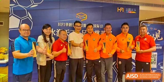 Four men stand together holding awards and giving thumbs up in front of a blue promotional banner for an international day event at Huafu International Department.