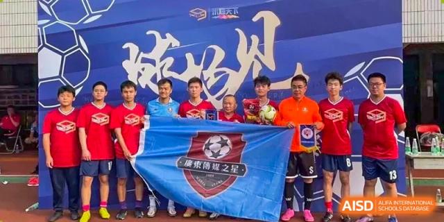 A group of athletes and officials pose behind a large blue sports banner featuring a soccer ball crest during a school competition at Huafu International Department.