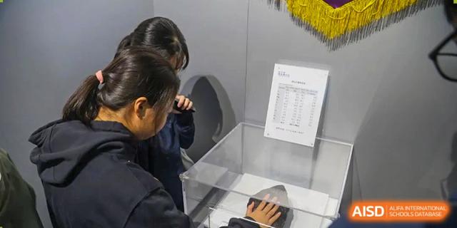 Students observe a scientific specimen or artifact protected inside a clear display case with an informational chart at Huafu International Department.